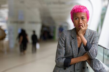 Young rebellious Asian businesswoman with pink hair thinking in the cityの写真素材