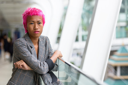 Young rebellious Asian businesswoman with pink hair looking at view of the city