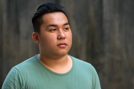 Face of young handsome overweight Asian man thinking outdoorsの写真素材