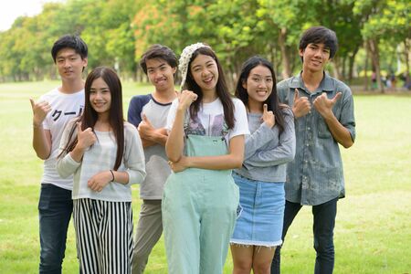 Happy young group of friends giving thumbs up together at the parkの写真素材