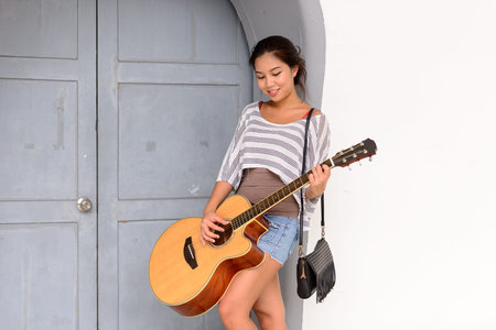 Happy young beautiful Asian woman playing guitar outdoors