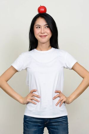 Young beautiful Asian woman thinking with apple on top of headの写真素材