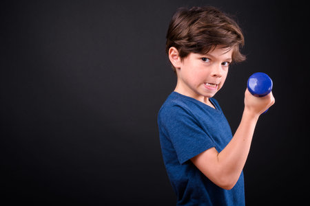 Portrait of funny young handsome boy exercising with dumbbells