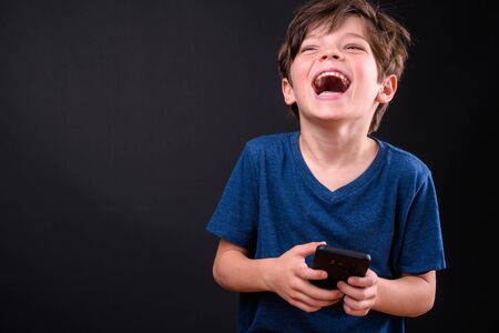 Portrait of happy young handsome boy laughing while using phoneの写真素材