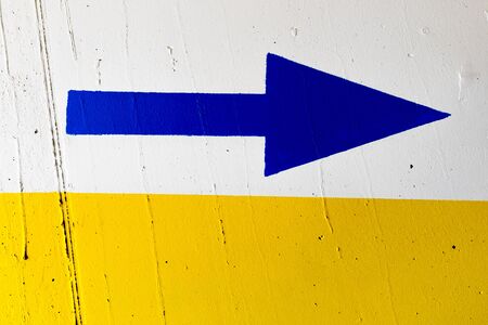 Blue arrow painted on white and yellow wallの写真素材