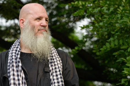 Mature bald hipster man with long beard at the park outdoors