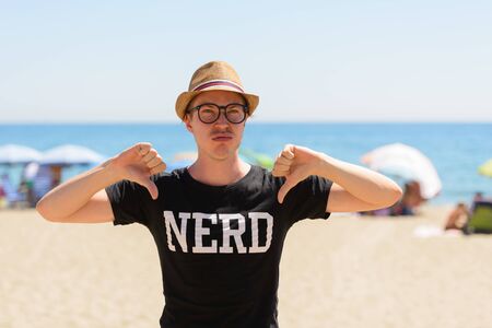 Stressed young nerd tourist man giving thumbs down at the beachの写真素材