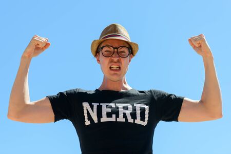 Young nerd tourist man flexing both arms against blue skyの写真素材