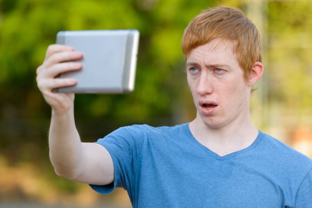 Face of man with red hair taking selfie with digital tablet in the parkの写真素材