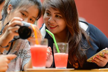 Happy young Asian women as friends using camera together at the coffee shop outdoorsの写真素材