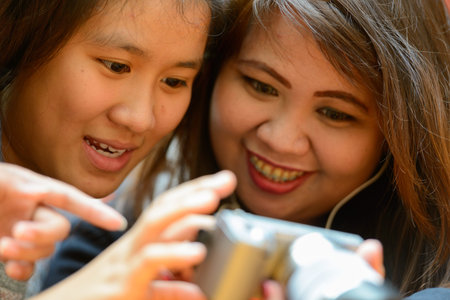Happy young Asian women as friends using camera together at the coffee shop outdoors