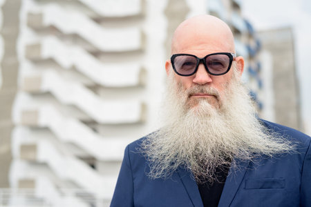 Face of mature bald bearded businessman in suit wearing sunglasses outdoors