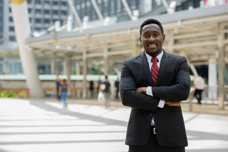 Happy young African businessman with arms crossed in the city outdoors