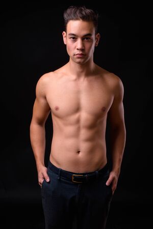 Young handsome multi ethnic man shirtless against black backgroundの写真素材