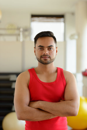 Young handsome bearded Indian man with arms crossed ready for gym