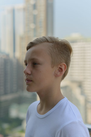 Face of young handsome boy with blond hair thinking against view of the city