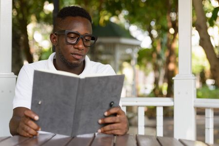 Young African man as student with eyeglasses reading book at the parkの写真素材