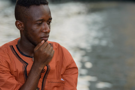 Stressed young African man thinking and looking sad at river in the city