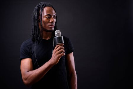 Portrait of young handsome African man with dreadlocks using microphoneの写真素材