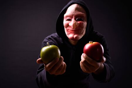 Studio shot of young Asian man with hoodie and horror mask against black backgroundの写真素材