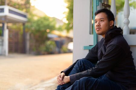 Young Asian man thinking while sitting in the streets outdoorsの写真素材