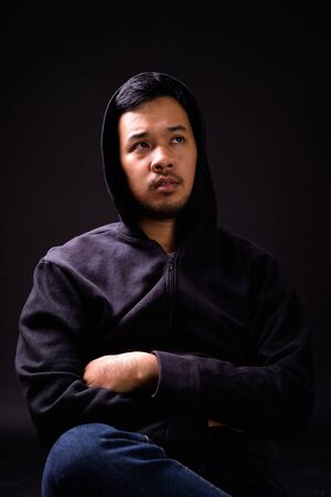 Portrait of young Asian man with hoodie thinking while sitting on chairの写真素材