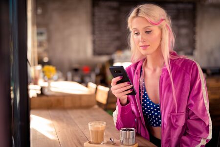 Young beautiful blonde woman using phone and sitting at the coffee shopの写真素材