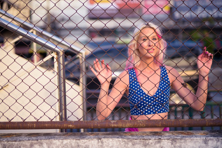Young beautiful blonde woman looking through chain link fence outdoors