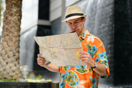 Young handsome tourist man reading map in the city outdoors