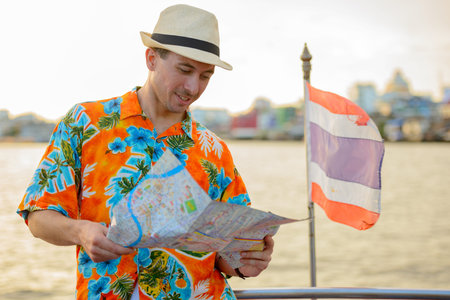 Young handsome tourist man with map at pier against view of the riverの写真素材