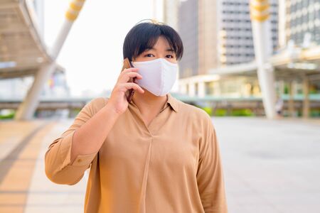 Overweight Asian woman with mask talking on the phone at skywalk bridgeの写真素材