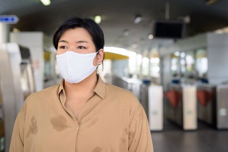 Overweight Asian woman thinking with mask for protection from corona virus outbreak at the sky train stationの写真素材