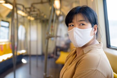 Overweight Asian woman with mask thinking while sitting with distance inside the trainの写真素材