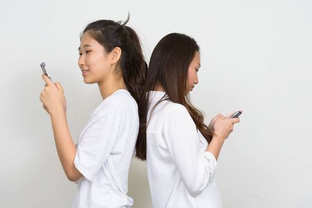 Two young beautiful Asian women as friends using phone togetherの写真素材