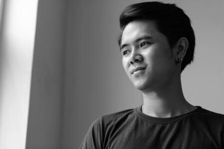 Portrait of young Asian man by the window indoors in black and whiteの写真素材