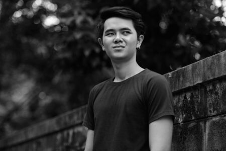 Portrait of happy young Asian man thinking outdoorsの写真素材