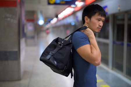 Portrait of young Asian man with bag at the subway stationの写真素材
