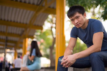 Portrait of young Asian man sitting at the bus stopの写真素材