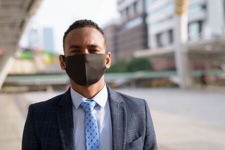 Face of young African businessman in suit wearing mask for protection from corona virus outbreak in the cityの写真素材
