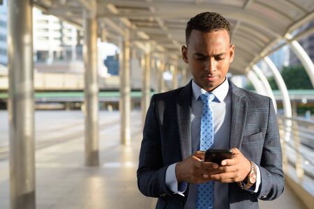 Young handsome African businessman using phone in the cityの写真素材
