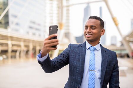 Happy young handsome African businessman taking selfie in the city outdoorsの写真素材