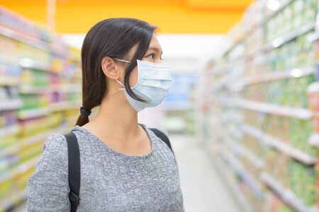 Profile view of young Asian woman wearing mask and shopping with distance at the supermarketの写真素材