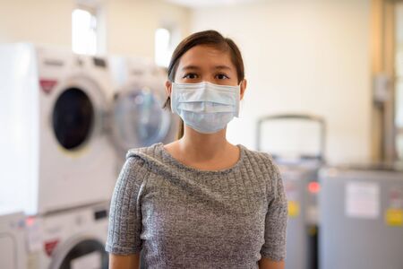Young Asian woman wearing mask at the laundromat for protection from corona virus outbreakの写真素材