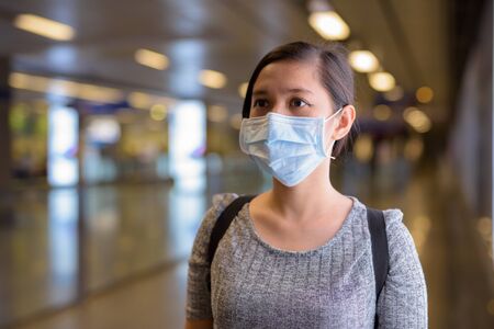 Young Asian woman with mask standing by the light at the subway train stationの写真素材