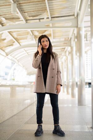 Full body shot of young beautiful Indian businesswoman talking on the phone in the cityの写真素材