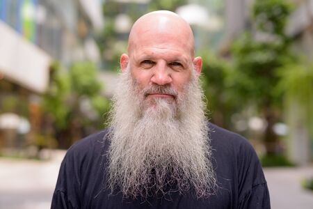 Face of mature handsome bald bearded man with nature in the cityの写真素材