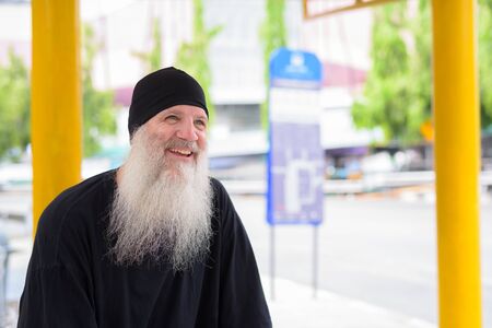 Happy mature handsome bearded hipster man sitting at the bus stopの写真素材