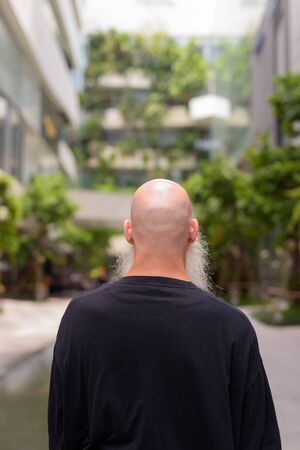 Rear view of mature bald bearded man looking at nature in the cityの写真素材