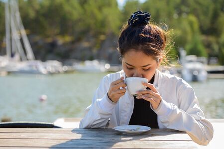 Young beautiful Asian tourist woman drinking coffee by the pierの写真素材