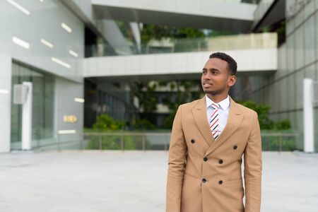 Happy young handsome African businessman thinking in the cityの写真素材